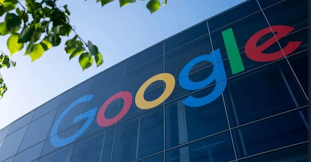 Fachada espelhada de um prédio comercial com o logotipo colorido do Google em destaque sob céu azul.